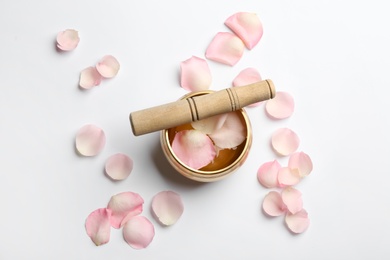 Photo of Golden singing bowl with petals and mallet on white background, flat lay. Sound healing