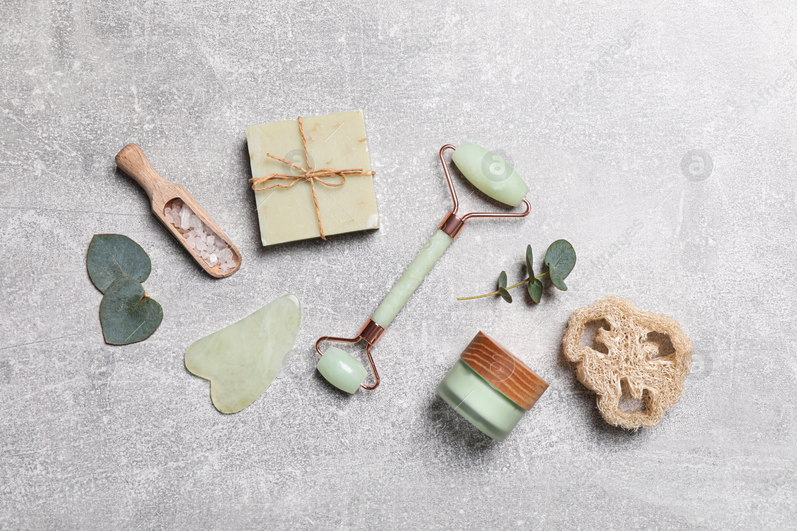 Photo of Flat lay composition with face roller and cosmetic products on light grey stone table