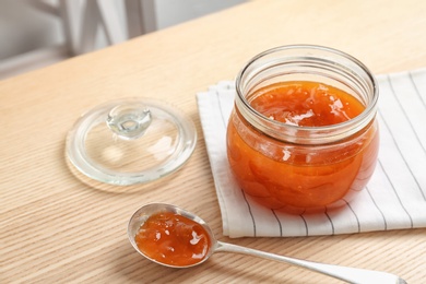 Jar and spoon with sweet jam on wooden table