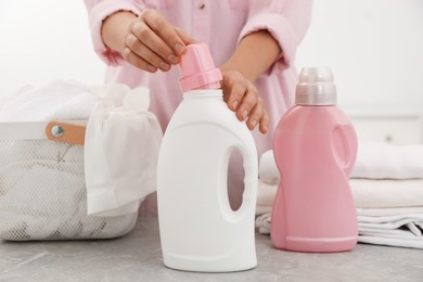 Photo of Woman opening bottle of laundry detergent at home, closeup