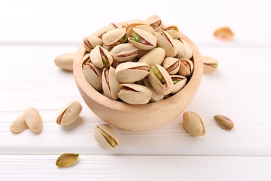 Tasty pistachios in bowl on white wooden table