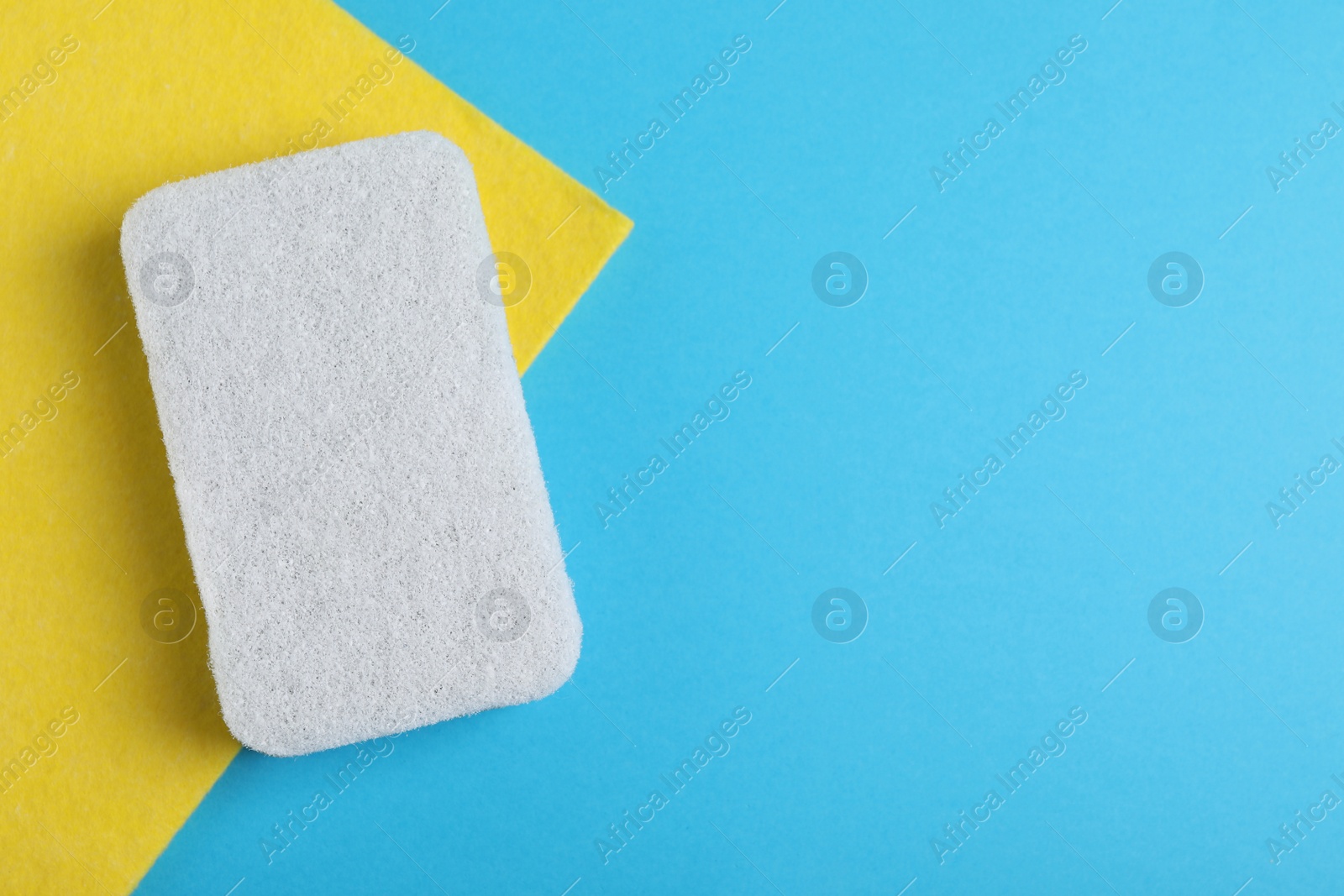 Photo of White sponge and yellow rag on light blue background, top view. Space for text