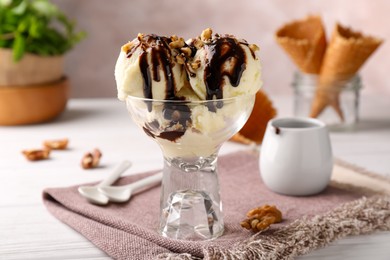 Photo of Glass dessert bowl of tasty ice cream with chocolate topping and nuts served on white table, closeup