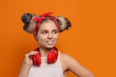 Beautiful woman with braided double buns and headphones on orange background, space for text
