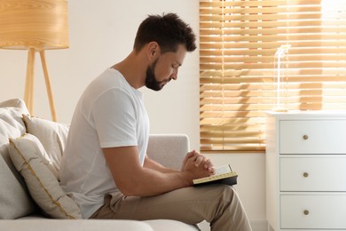 Photo of Religious man with Bible praying indoors. Space for text