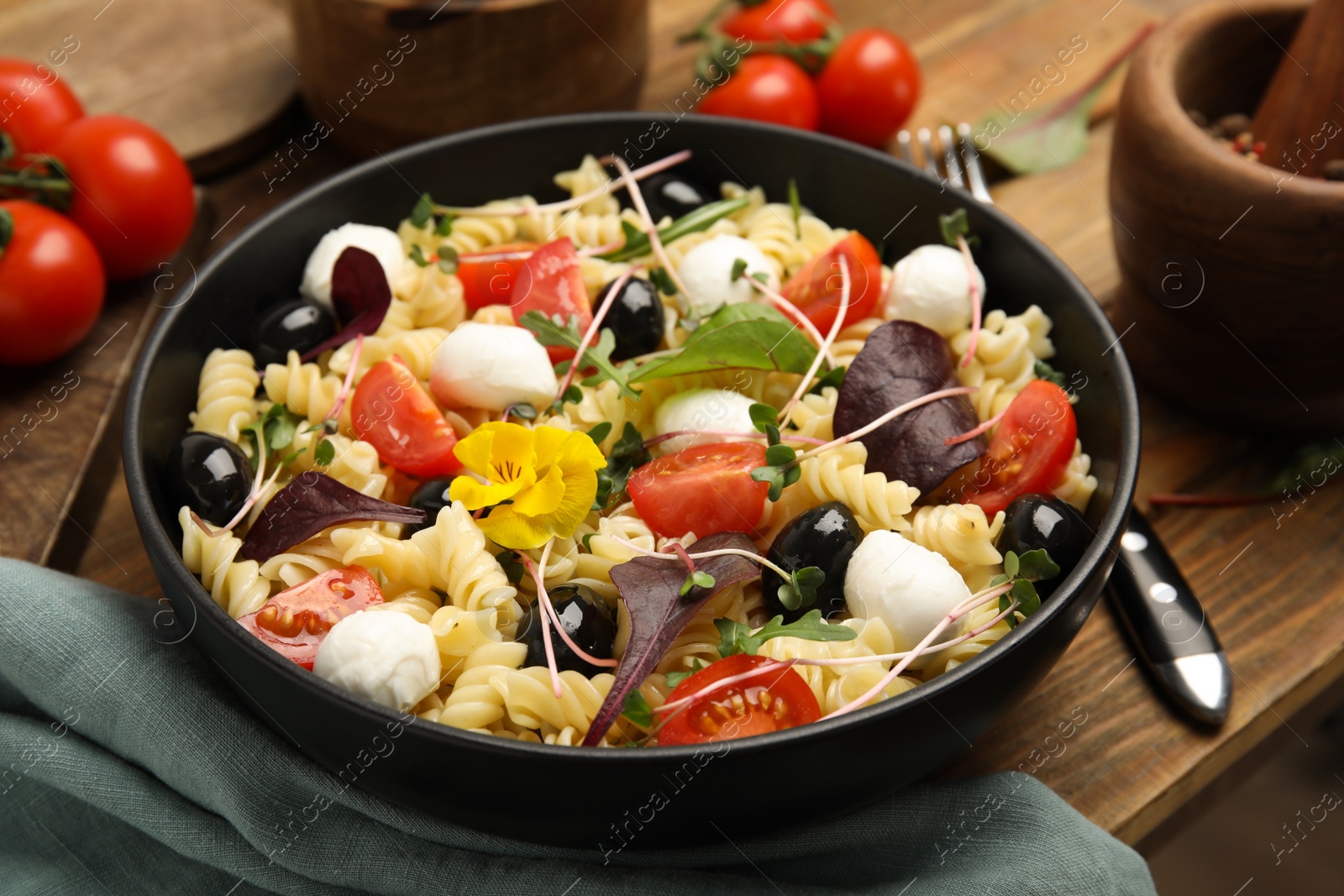 Photo of Bowl of delicious pasta with tomatoes, olives and microgreens on wooden table, closeup