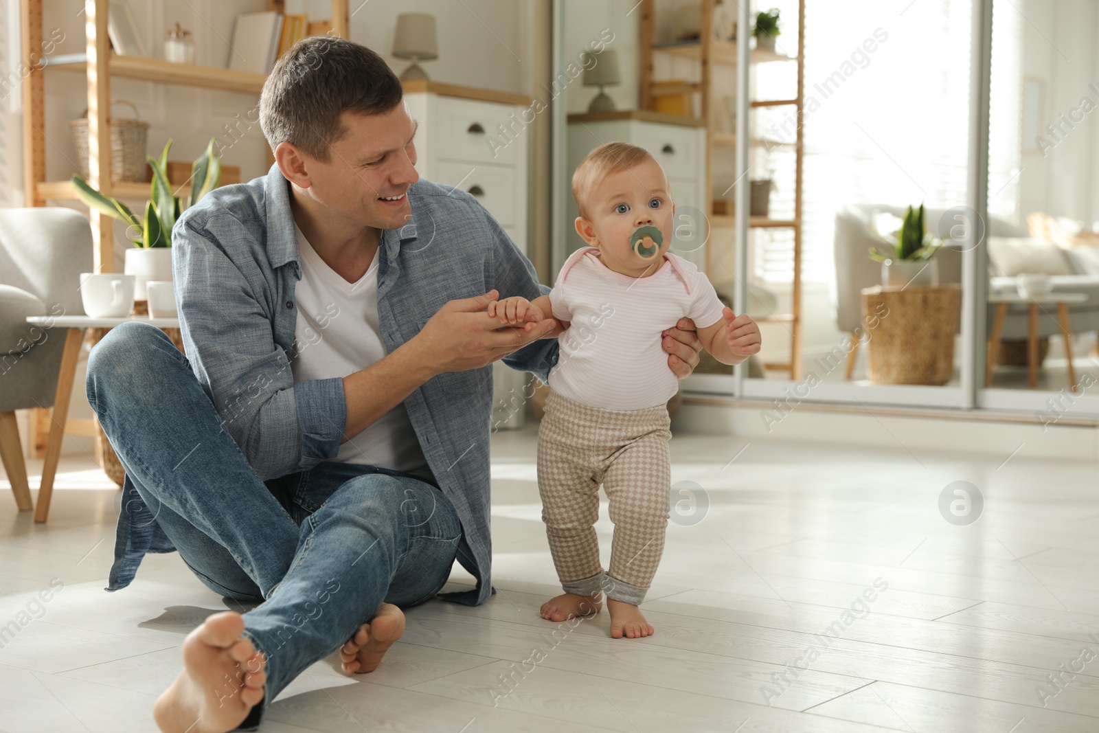 Photo of Father supporting his baby daughter while she learning to walk at home