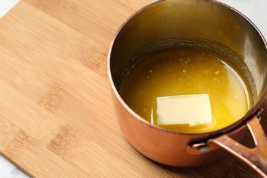Photo of Saucepan with melting butter on wooden board, closeup. Space for text