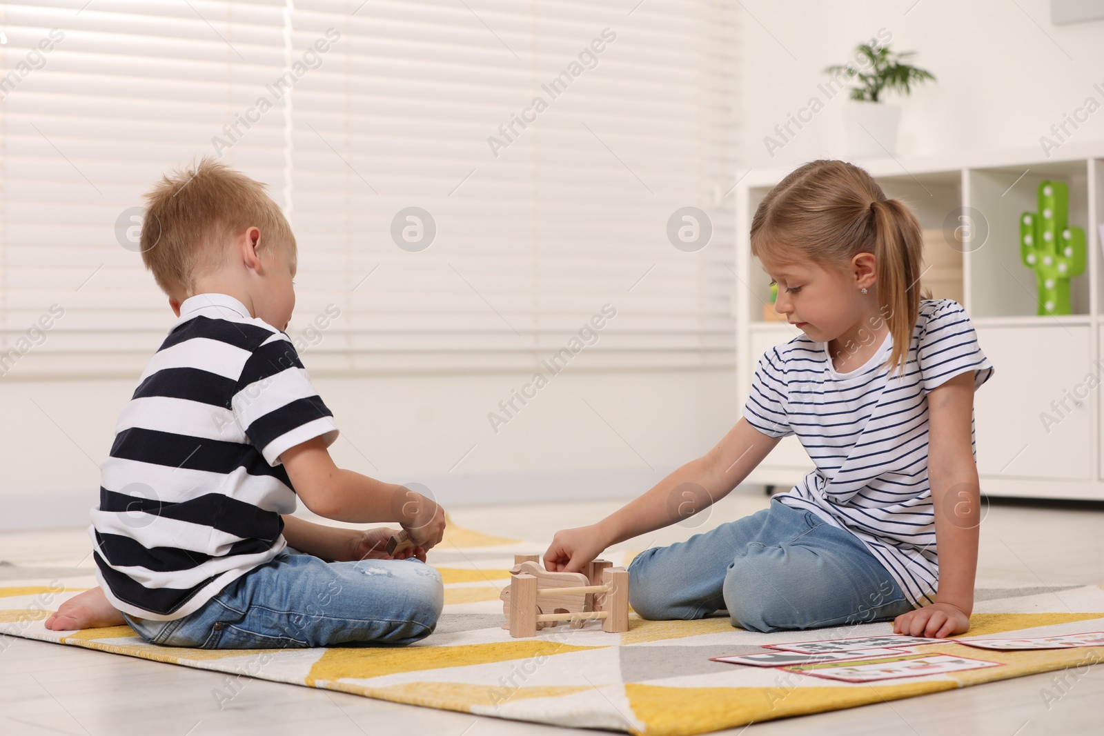 Photo of Little boy and girl playing with set of wooden animals indoors. Children's toys