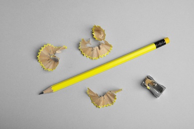 Photo of Pencil, sharpener and shavings on grey background, flat lay