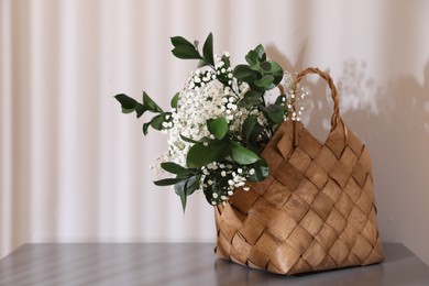 Photo of Stylish wicker basket with bouquet of flowers on wooden table indoors, space for text