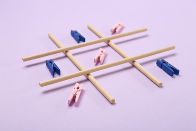 Photo of Tic tac toe game made with clothespins on lilac background