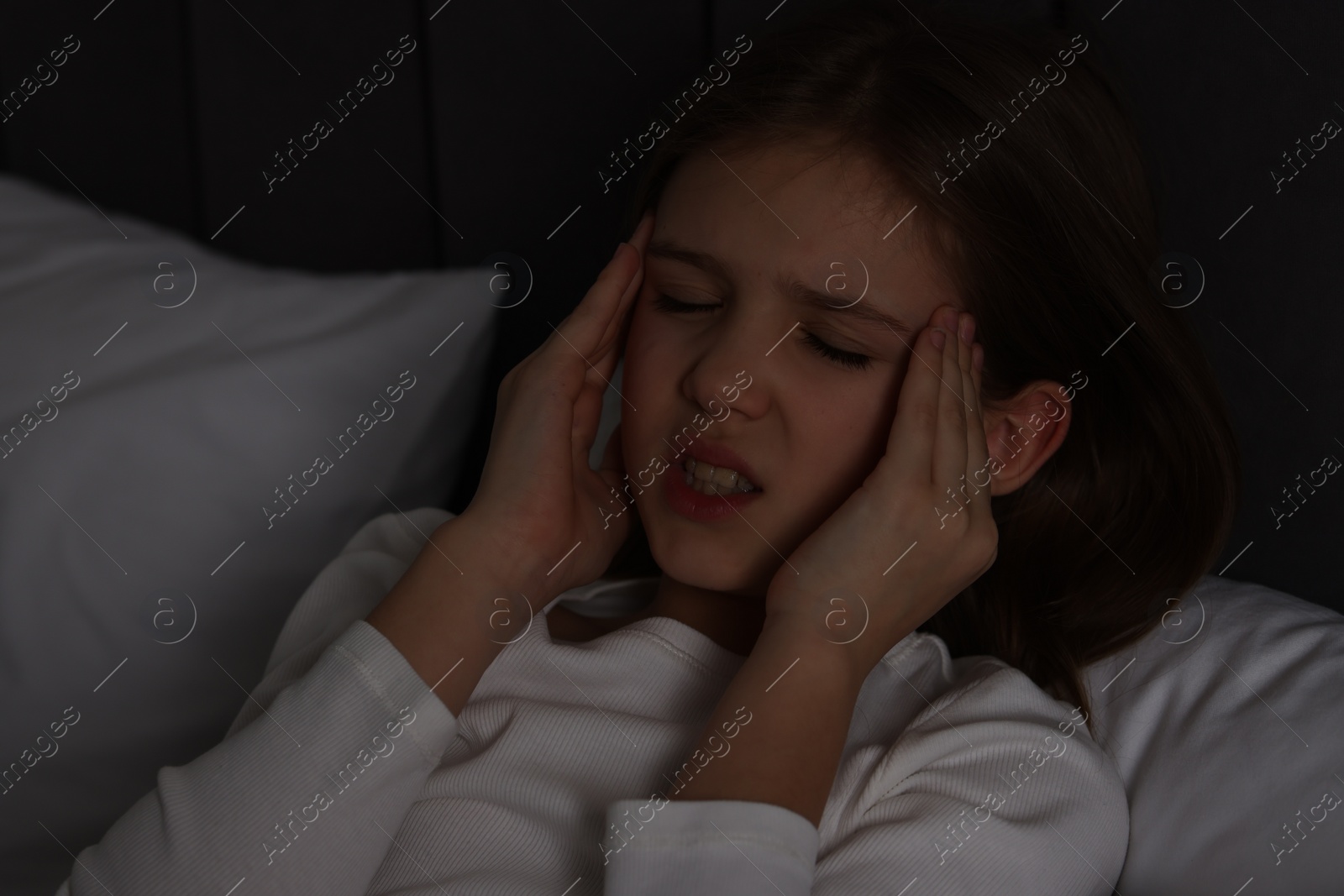 Photo of Little girl suffering from headache in bed at night