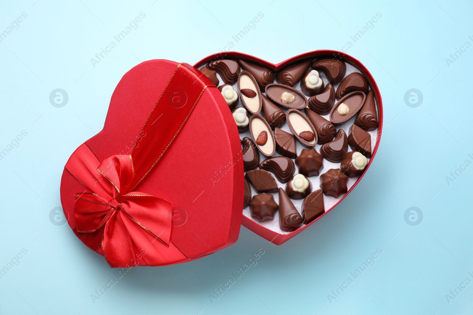 Photo of Heart shaped box with delicious chocolate candies on light blue background, top view