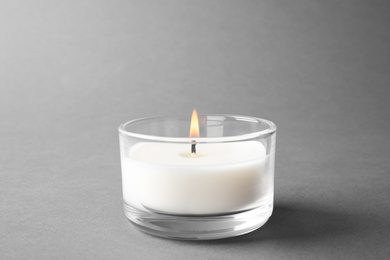Photo of Burning small wax candle in glass holder on grey background