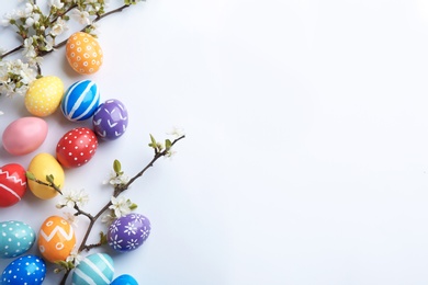 Photo of Composition with painted Easter eggs and blossoming branches on white background, top view