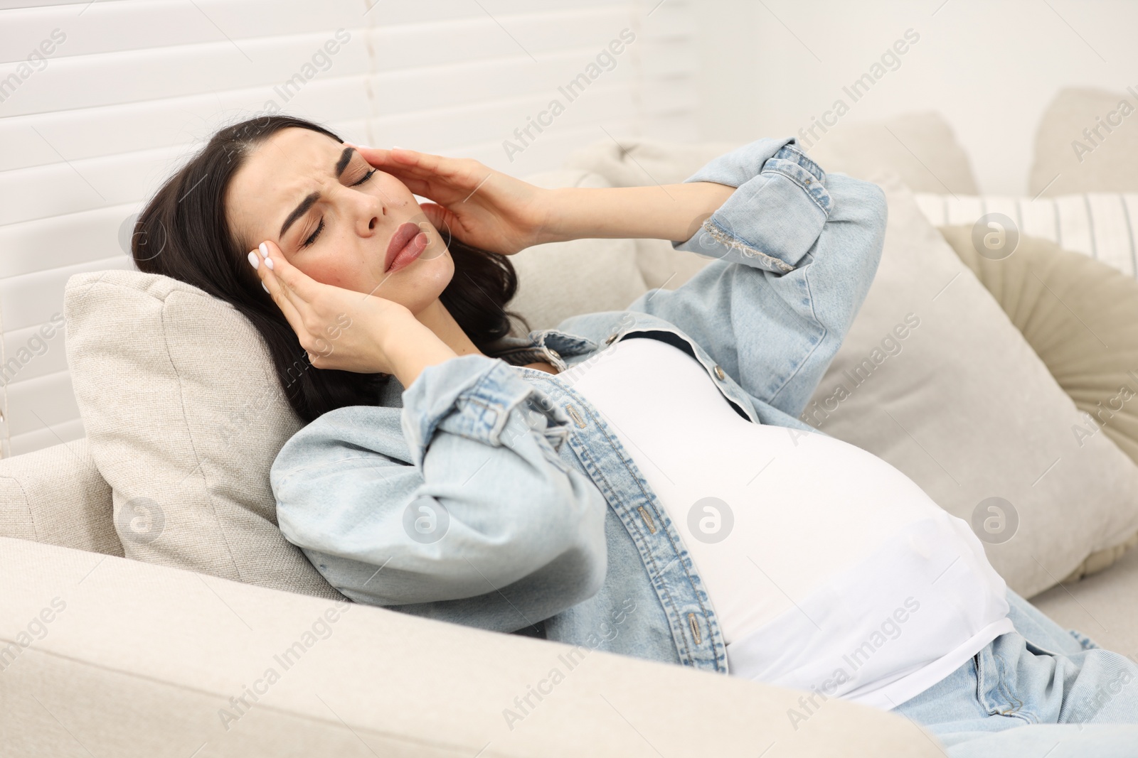 Photo of Pregnant woman suffering from headache on sofa at home