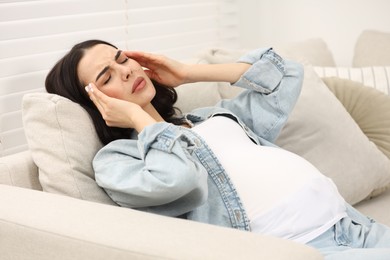 Pregnant woman suffering from headache on sofa at home