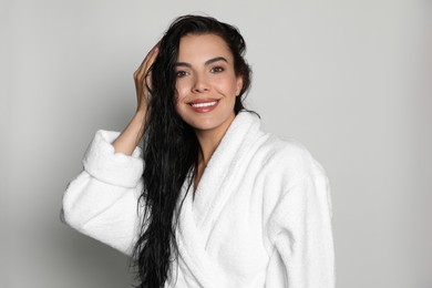 Beautiful young woman wearing bathrobe on light background