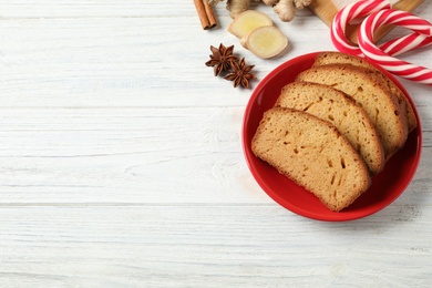 Slices of delicious gingerbread cake, ingredients and candy canes on white wooden table, flat lay. Space for text