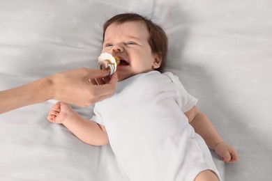 Photo of Mother giving pacifier to crying little baby on bed, closeup