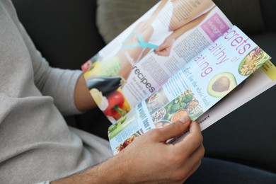 Photo of Man reading healthy food magazine on sofa at home, closeup