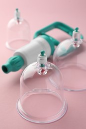 Photo of Plastic cups and hand pump on pink background, closeup. Cupping therapy