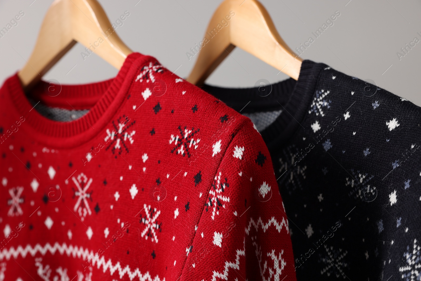 Photo of Christmas sweaters hanging on rack against light background, closeup