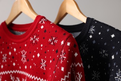 Christmas sweaters hanging on rack against light background, closeup