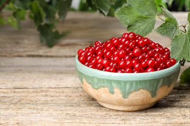 Photo of Ripe red currants in bowl on wooden table. Space for text