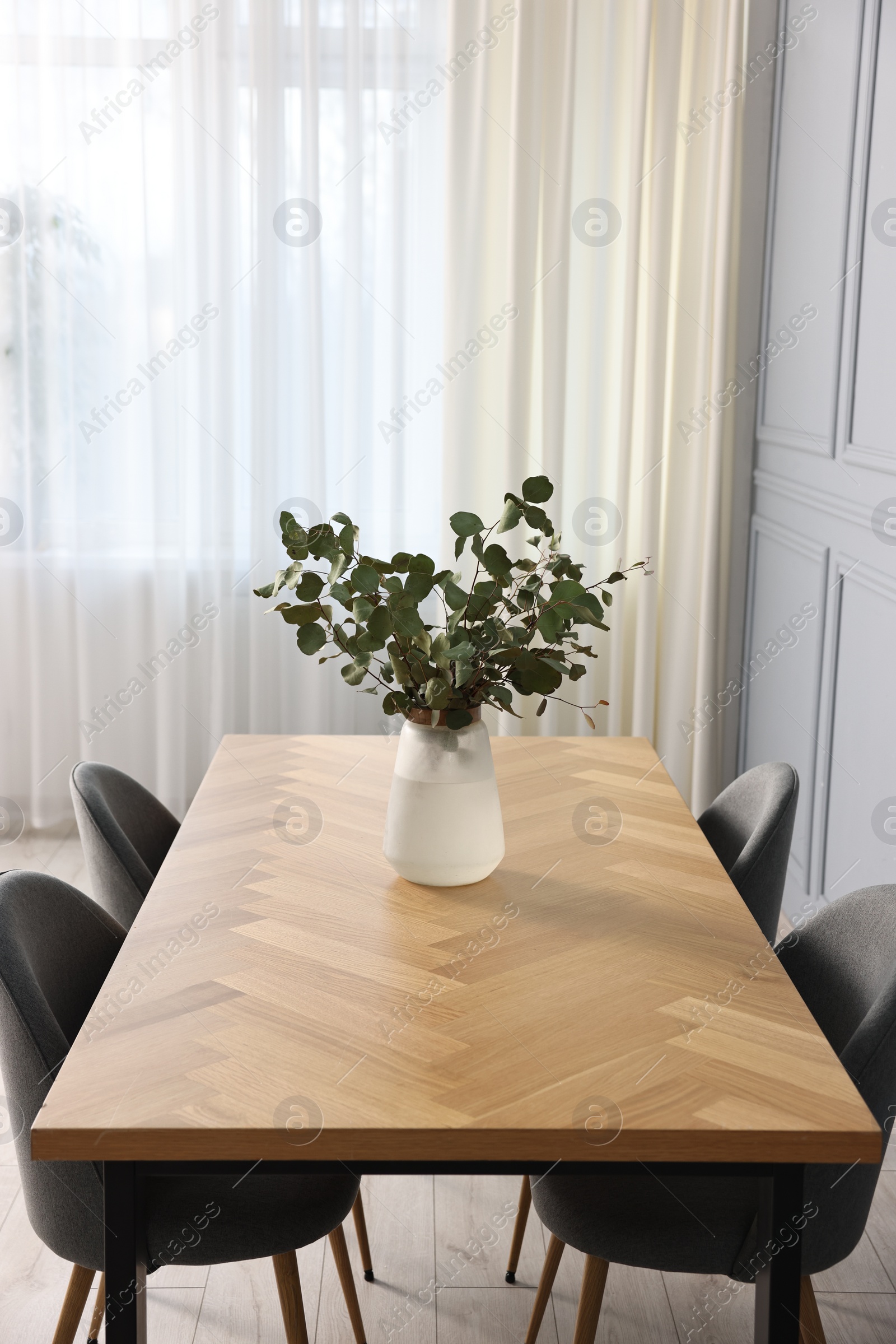 Photo of Soft chairs, table and vase with eucalyptus branches in stylish dining room