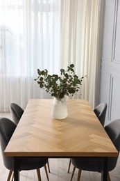 Photo of Soft chairs, table and vase with eucalyptus branches in stylish dining room