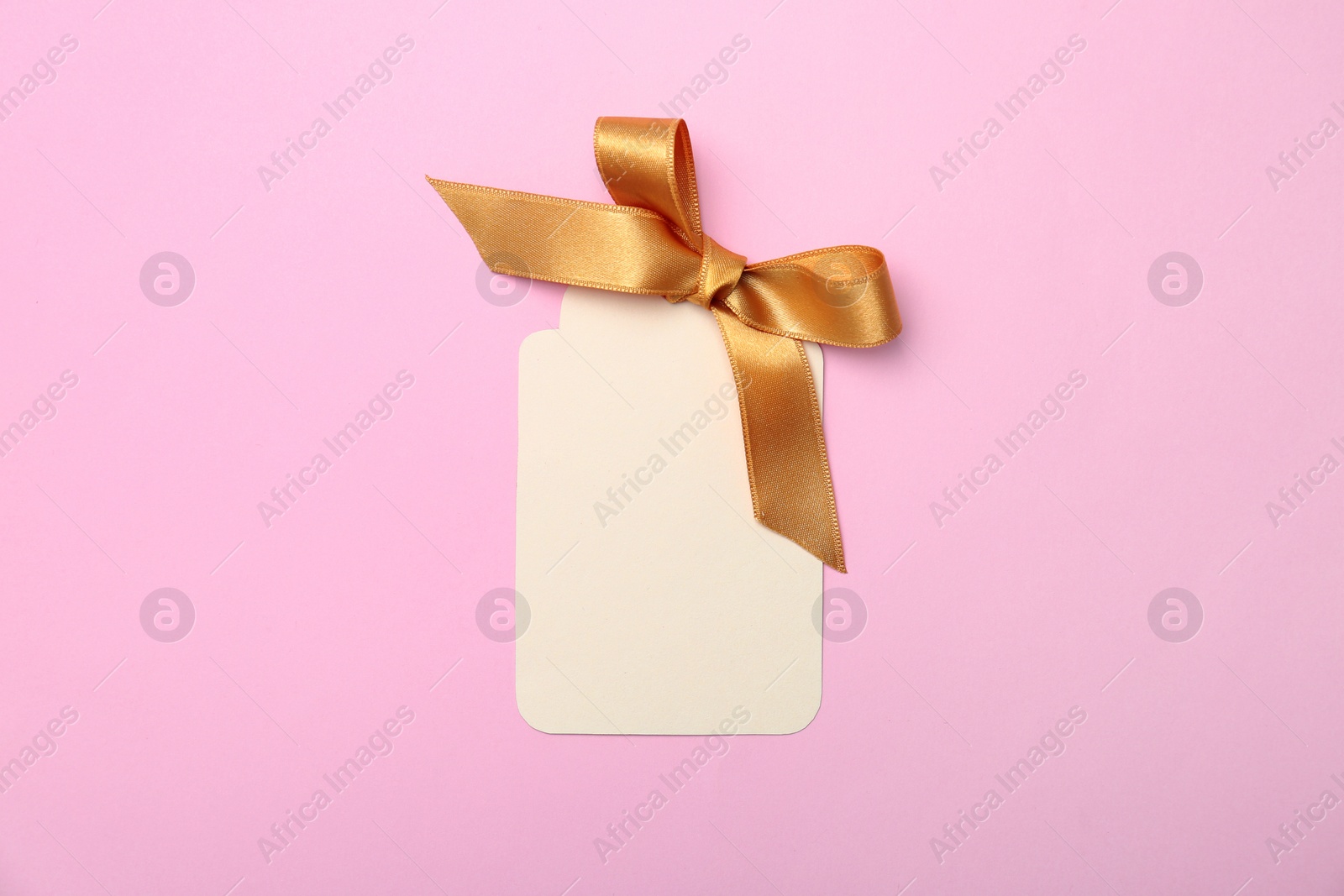 Photo of Blank gift tag with satin ribbon on color background, top view