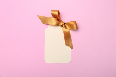 Blank gift tag with satin ribbon on color background, top view