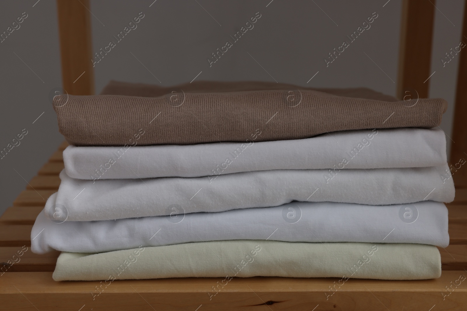 Photo of Different folded shirts on wooden shelf, closeup. Organizing clothes