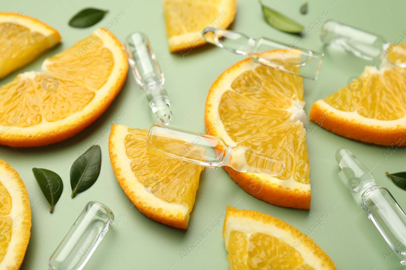 Photo of Skincare ampoules with vitamin C, slices of orange and leaves on light green background, closeup