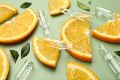 Skincare ampoules with vitamin C, slices of orange and leaves on light green background, closeup