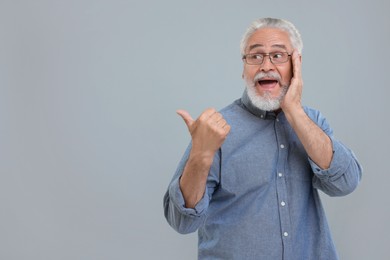Special promotion. Emotional senior man pointing at something on light grey background. Space for text