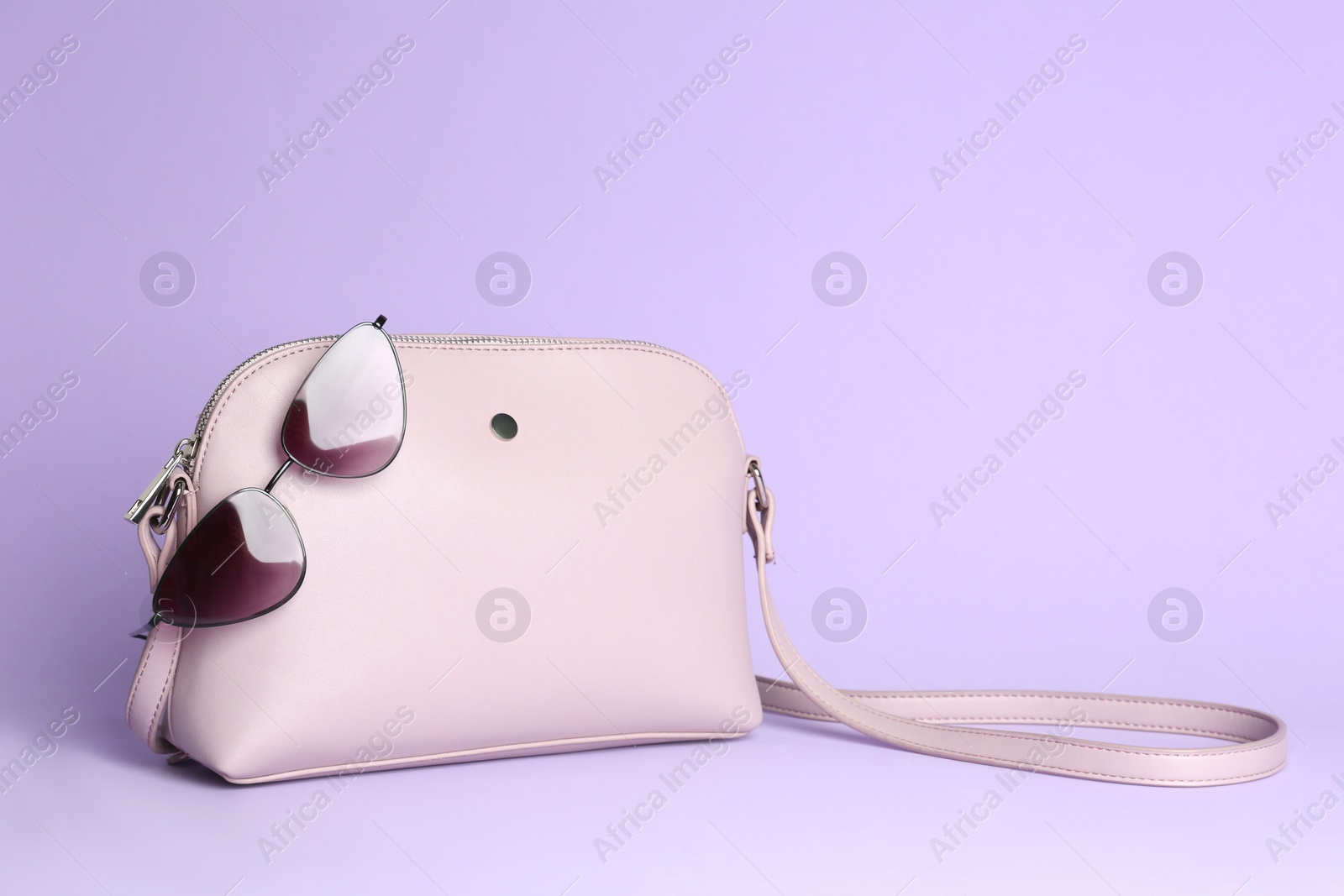 Photo of Stylish woman's bag and sunglasses on lilac background. Space for text