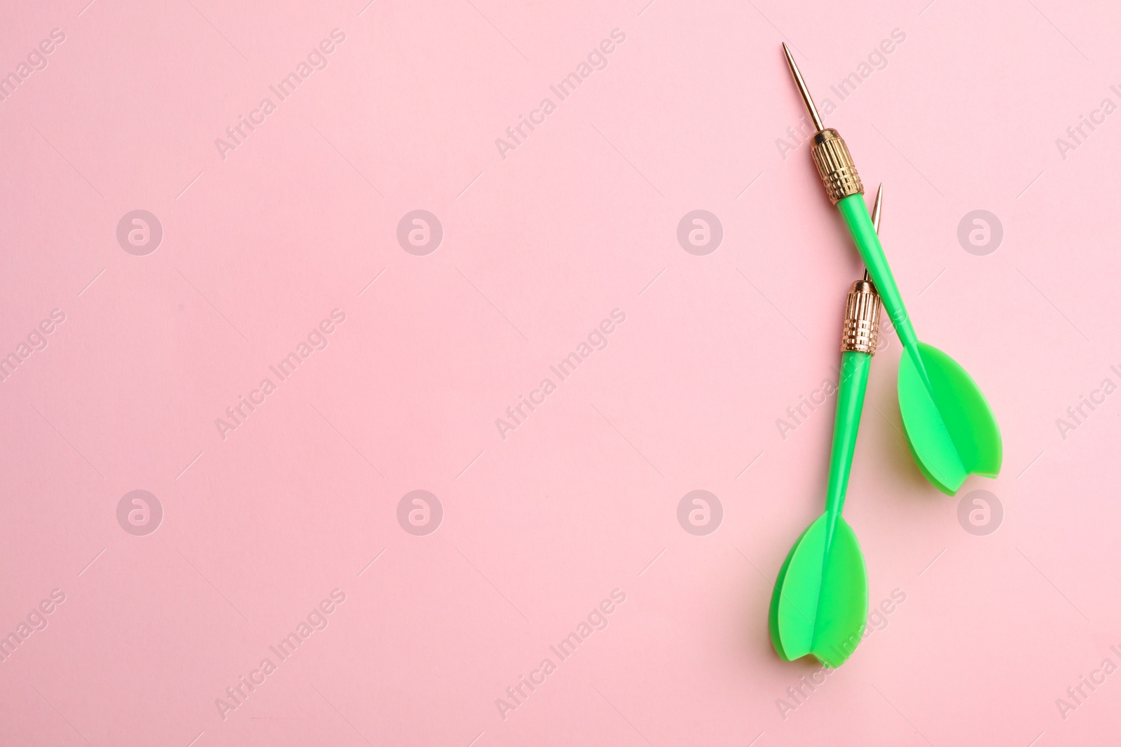 Photo of Green dart arrows on pink background, flat lay with space for text