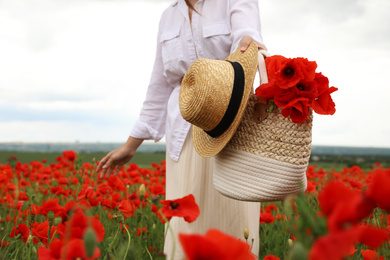 Photo of Woman holding straw hat and handbag with poppy flowers in beautiful field, closeup