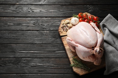 Photo of Board with raw turkey and ingredients on wooden background, top view. Space for text