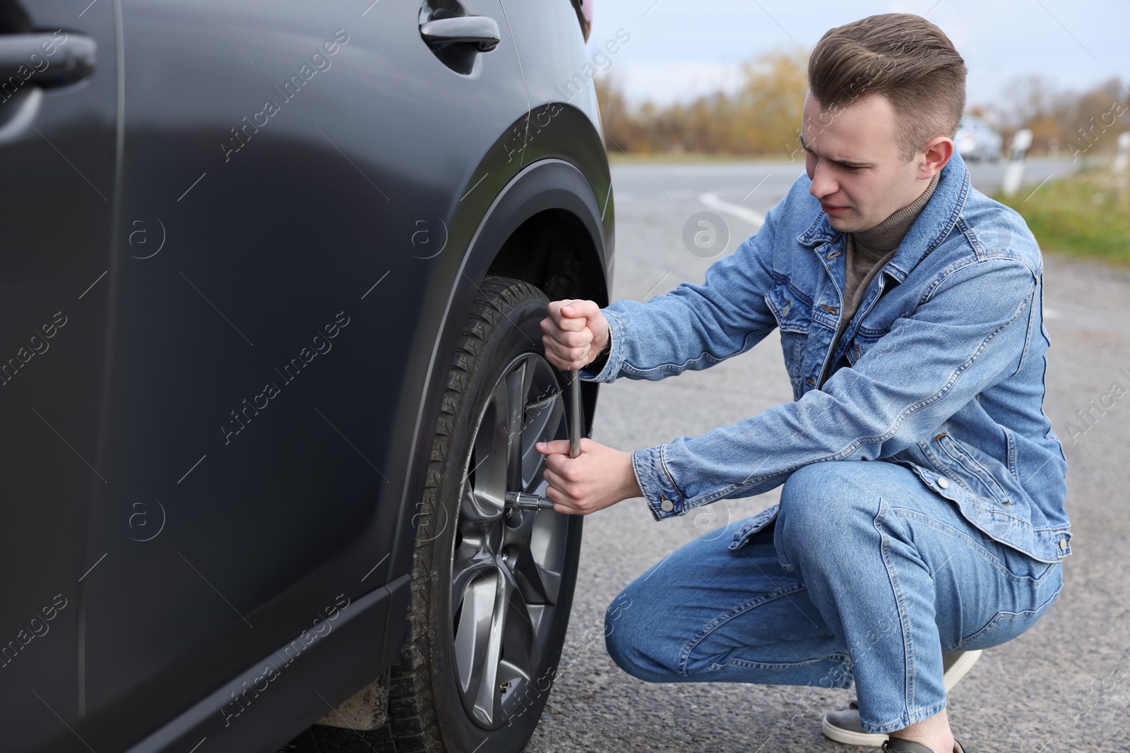 Photo of Young man changing tire of car on roadside