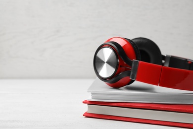 Photo of Modern headphones with hardcover books on wooden table. Space for text