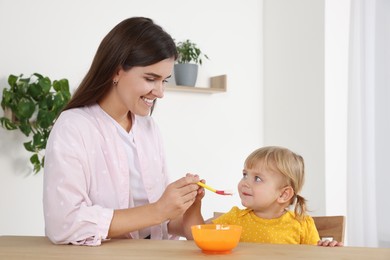 Photo of Mother feeding her cute little child with yogurt at wooden table indoors