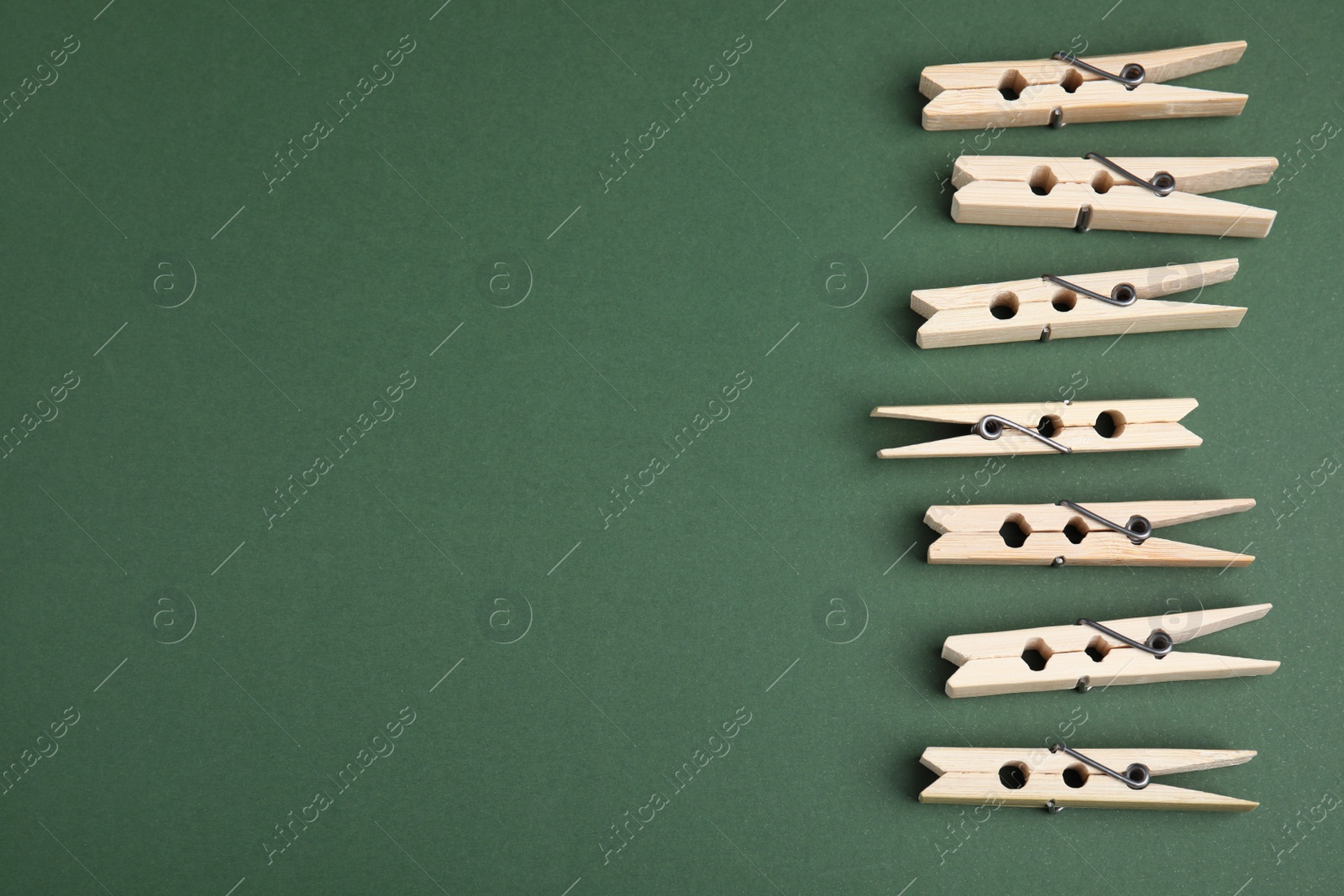 Photo of Wooden clothespins on dark green background, flat lay. Space for text