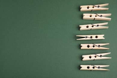 Photo of Wooden clothespins on dark green background, flat lay. Space for text