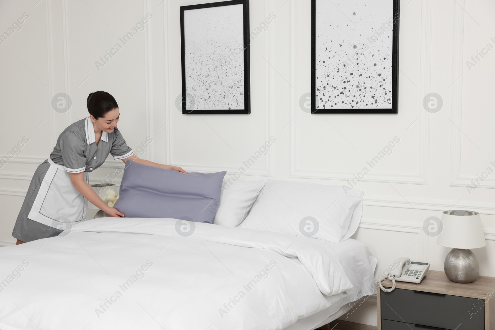 Photo of Young maid making bed in hotel room. Space for text