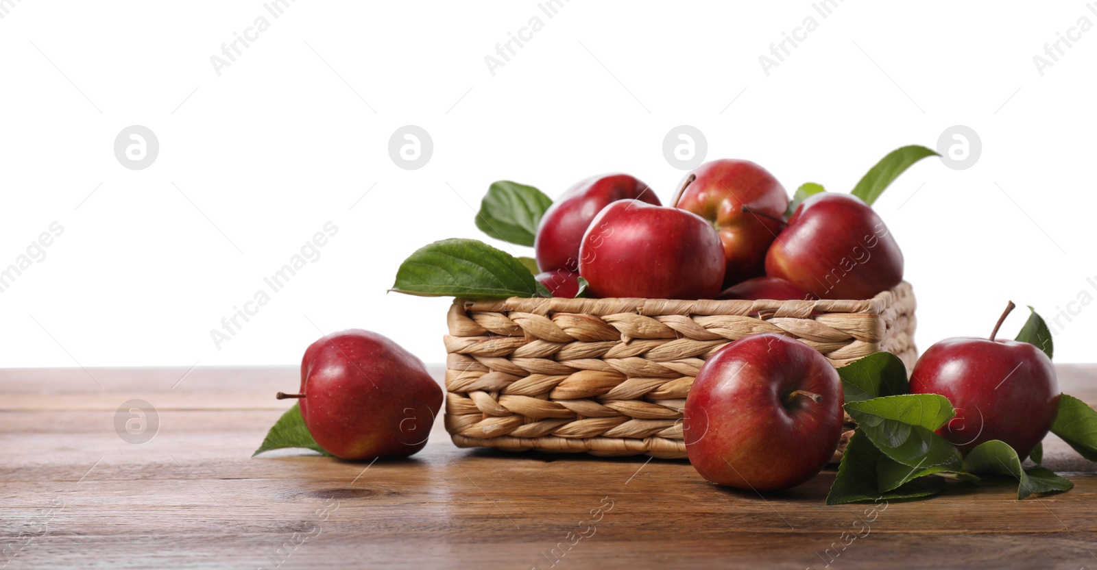 Photo of Fresh red apples and leaves in basket on wooden table against white background. Space for text