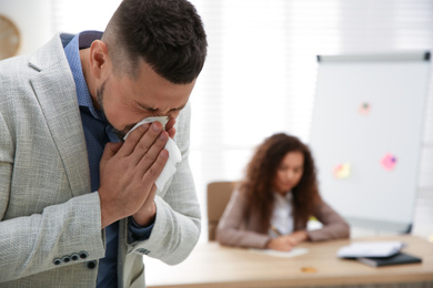 Photo of Sick man sneezing in office. Influenza virus
